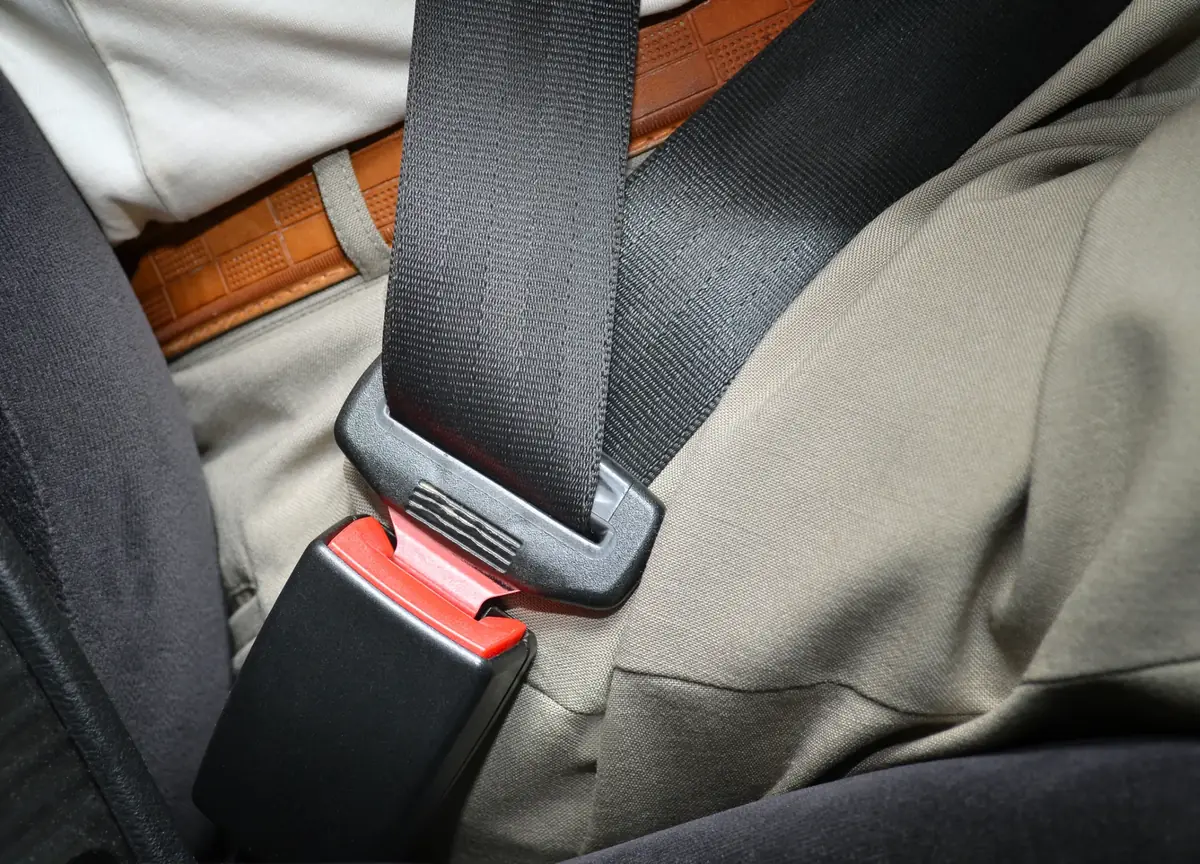 Seat belt fastened low across the hips of a seated occupant wearing khaki trousers