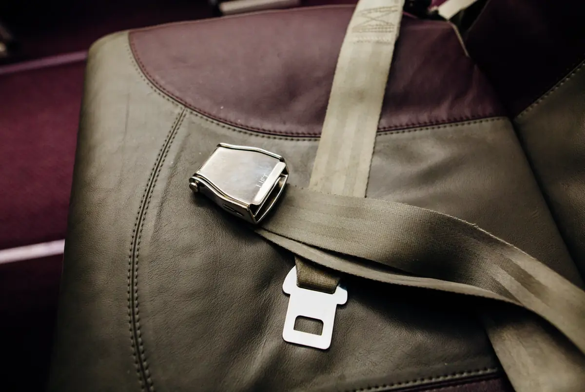 Polished metal lift-latch seat belt buckle with webbing resting on a leather passenger seat
