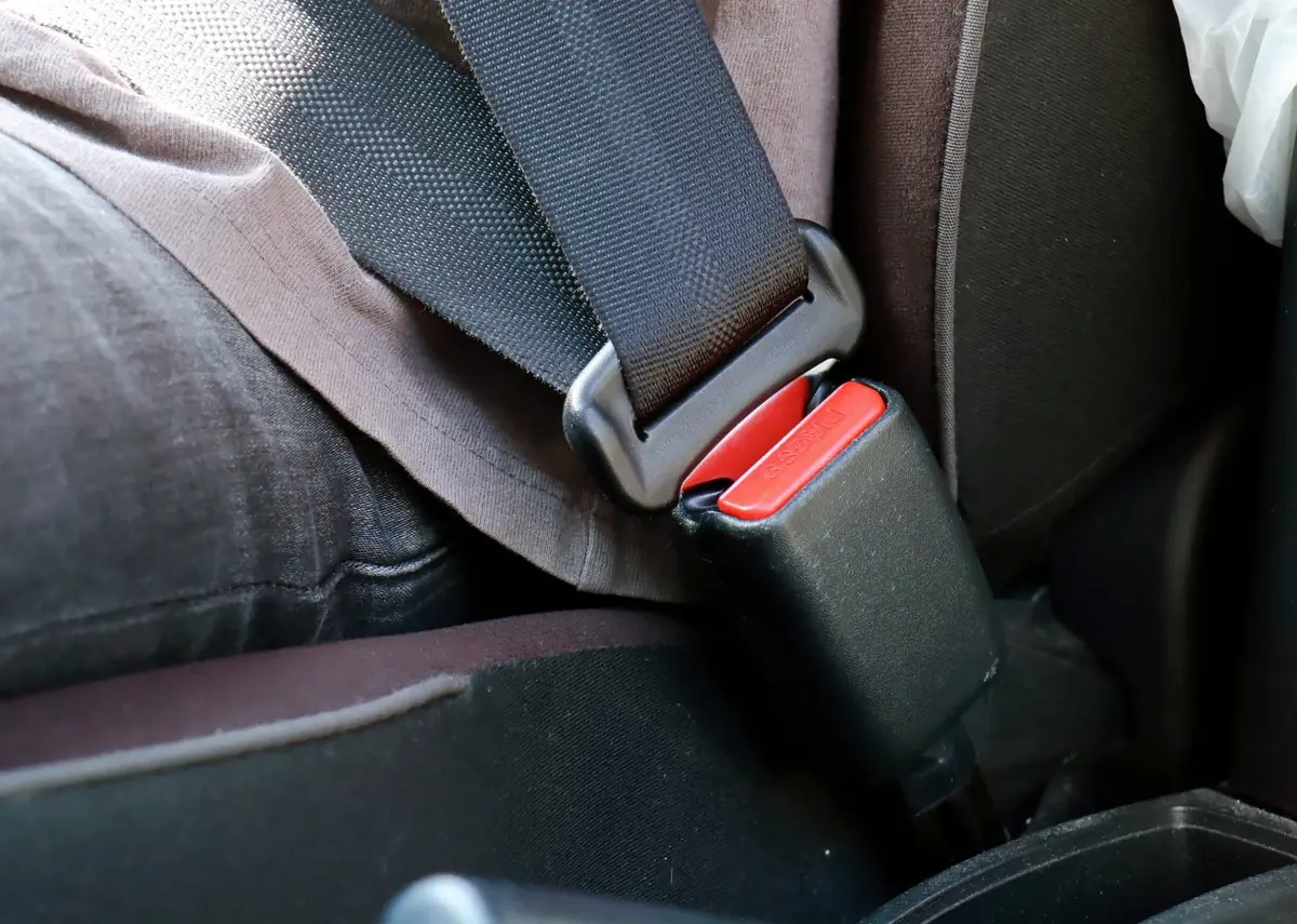 Seat belt buckle engaged beside a fabric vehicle seat with the webbing running up to the pillar