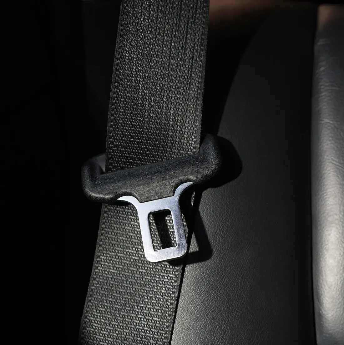 Seat belt webbing running through a moulded pillar loop against a dark vehicle interior