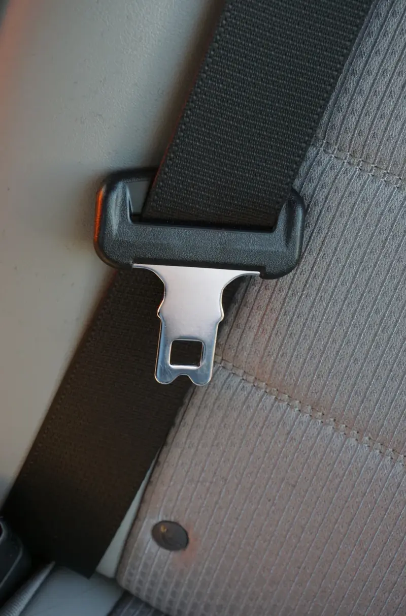 Chrome seat belt anchor plate seated in a black moulded pillar loop against grey seat trim