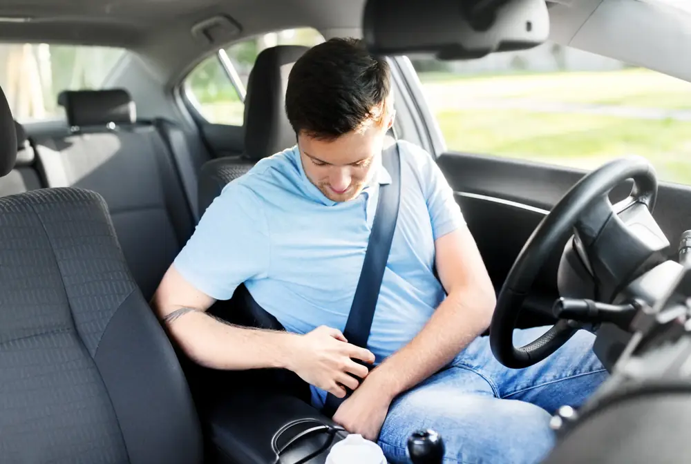 Driver in a light blue shirt fastening a three-point seat belt inside a passenger car