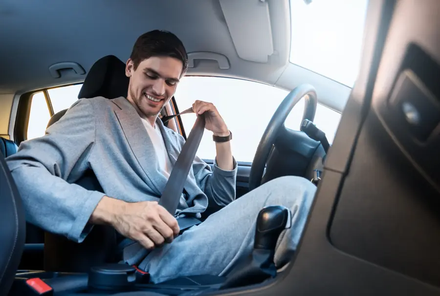 Person in a grey jacket drawing a seat belt across the body in a car's driver seat