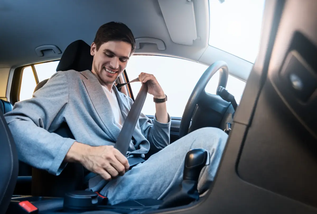 Occupant in a grey jacket drawing a seat belt across the body in a car's driver seat