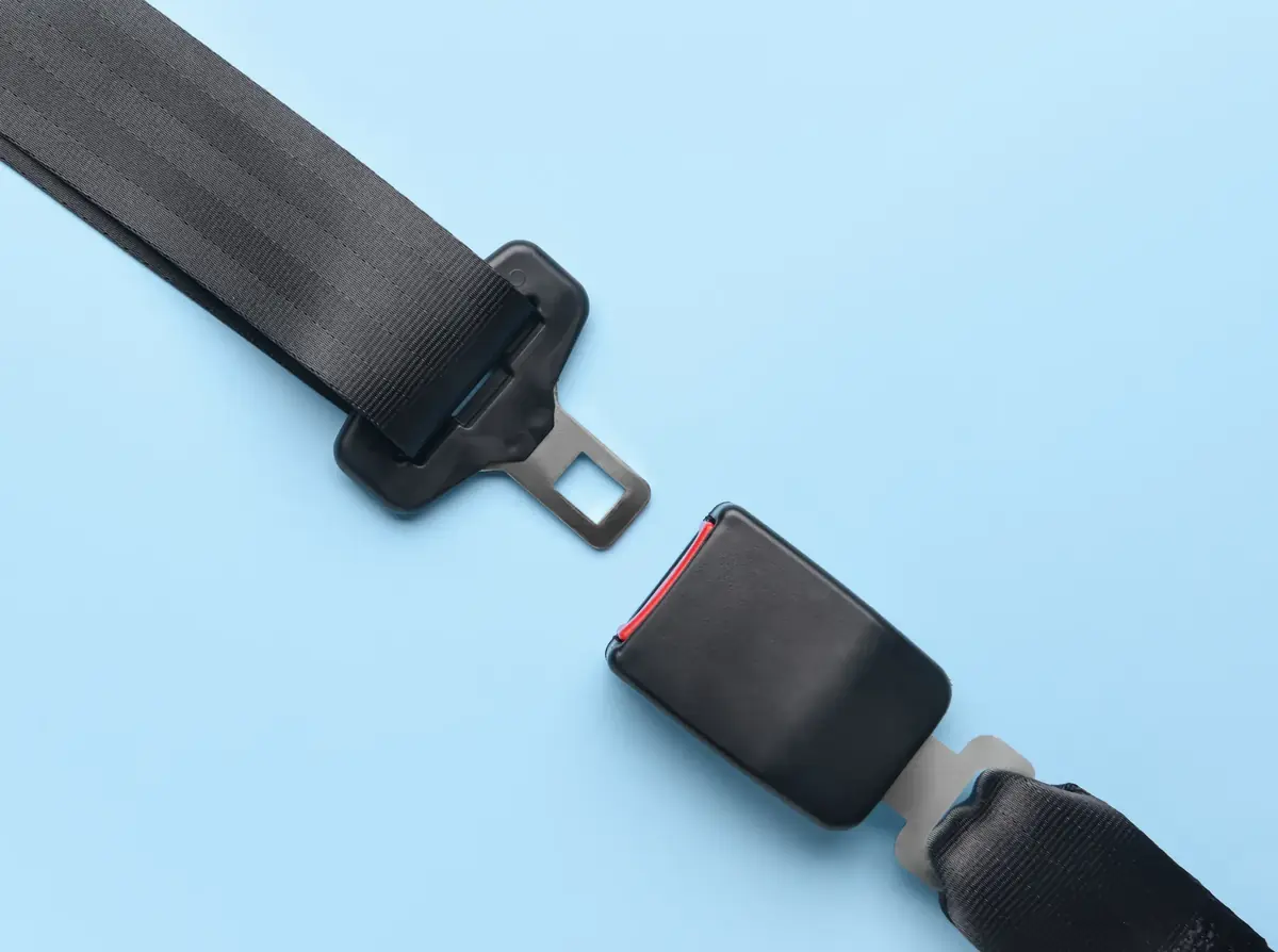Seat belt webbing with latch tongue on one side and the matching buckle on the other, laid out on a pale blue surface